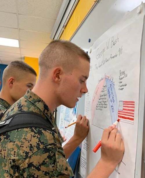 MMA cadets working at a whiteboard in a high school class.